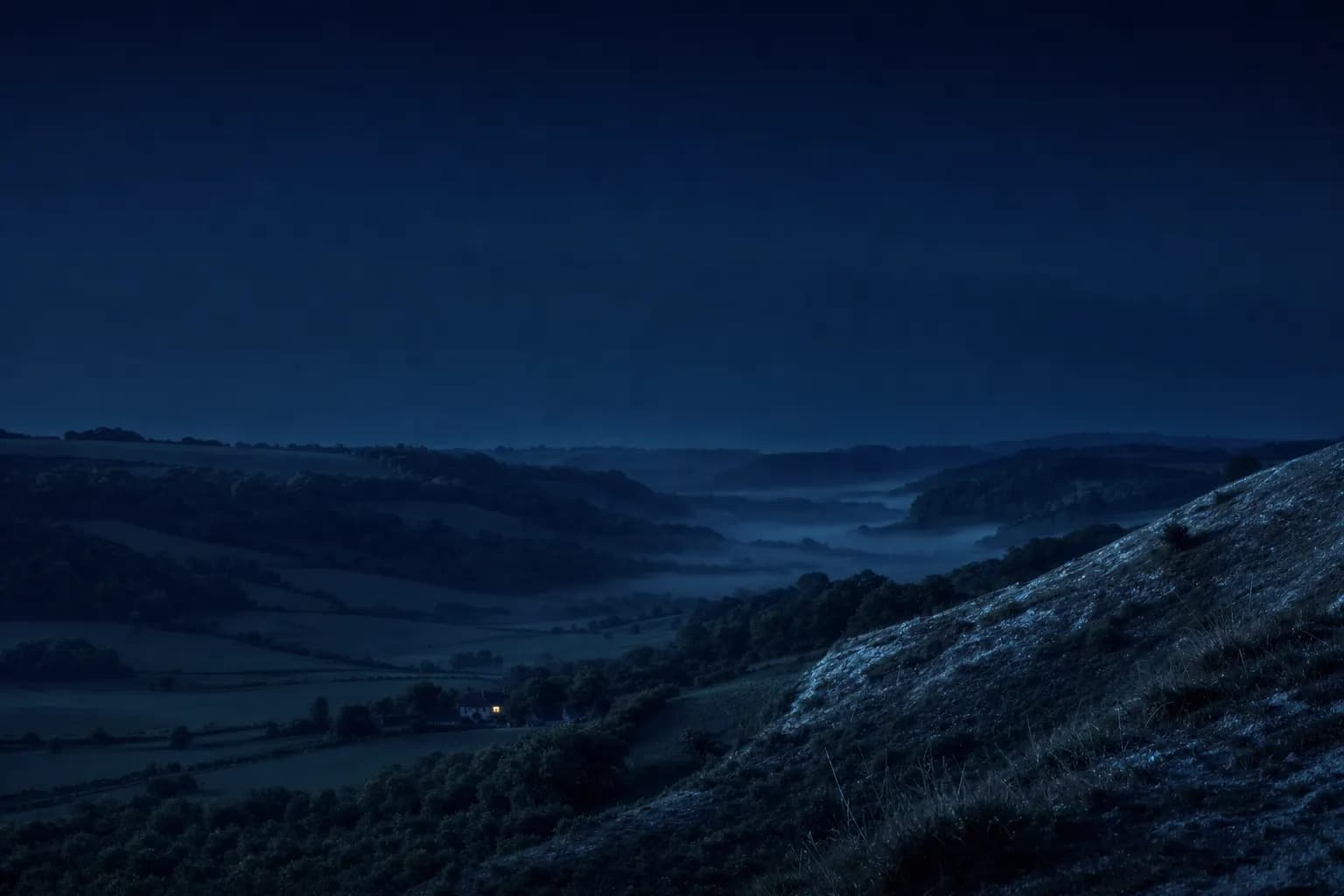 The Surrey Hills at blue hour seen from a chalk ridge, a lone gold-lit window in a valley farmhouse