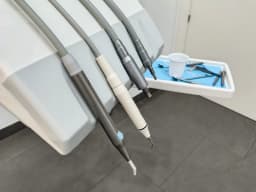 Dental handpieces hanging from a delivery unit beside a tray of instruments and a plastic rinsing cup