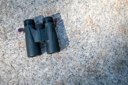 A pair of black binoculars lying on a speckled grey granite surface