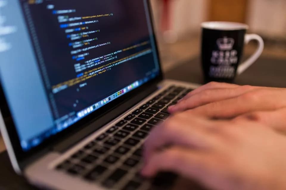 Close-up of hands typing PHP template code on a laptop keyboard beside a coffee mug