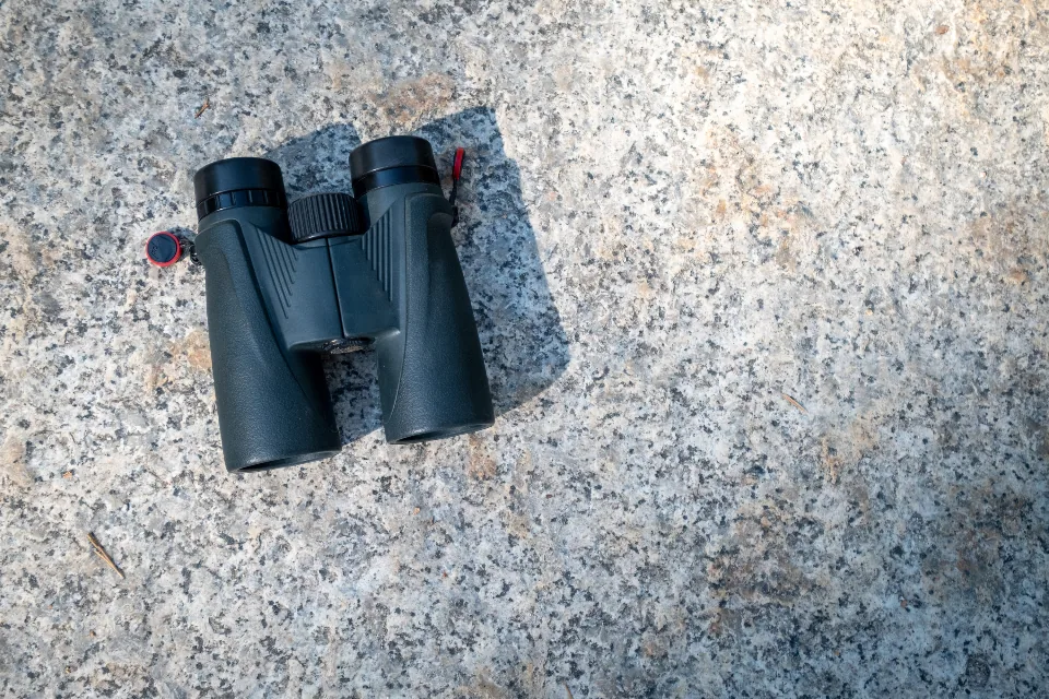A pair of black binoculars lying on a speckled grey granite surface