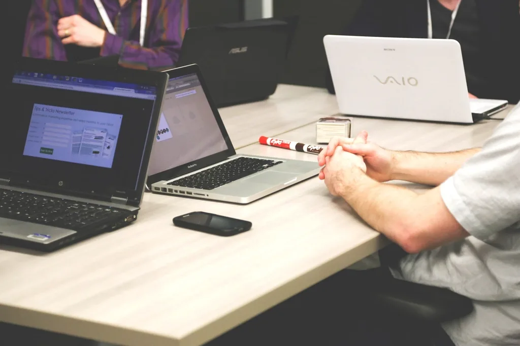Several open laptops on a meeting table, one showing a newsletter signup form, with people seated around it