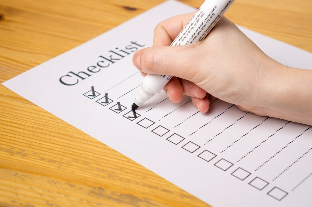 A hand ticking boxes on a printed checklist with a marker pen on a wooden desk